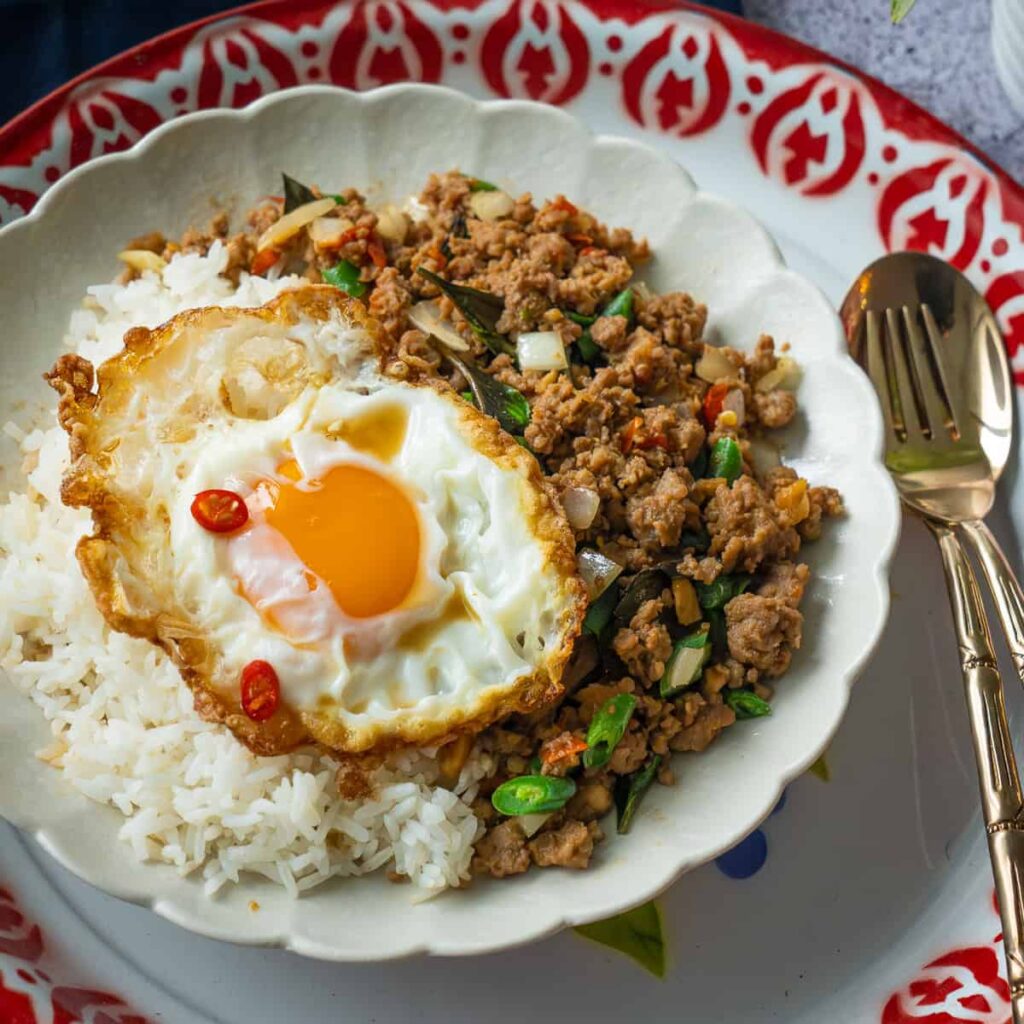 Stir-fried Thai basil chicken served with rice and a fried egg — “Pad Kra Pao – Mystic Thai Inspired.